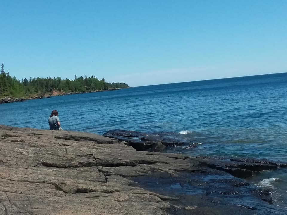 Mason sits on the lava flow beach looking out at a calm Lake Superior.